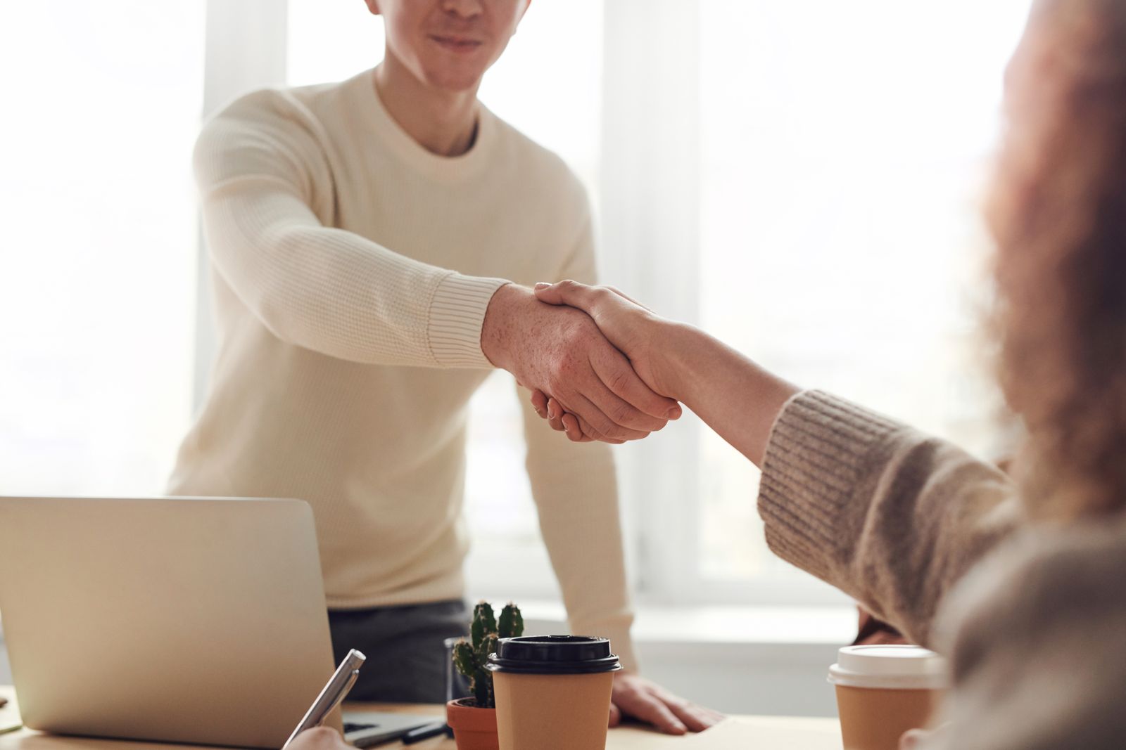 Two people shaking hands across a table during a meeting